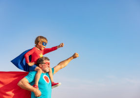 Superhero senior man and child playing outdoor. Super hero grandfather and boy having fun together against blue summer sky background. Family holiday concept. Happy Father\'s day